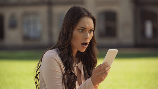 Shocked young woman looking at mobile phone in park.