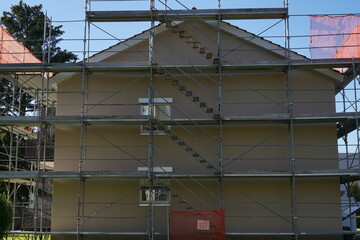 Residential apartment house in Switzerland with scaffolding and protective net, for reconstruction and installation of insulation. Around is of green vegetation.