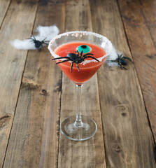 Terrifying red cocktail with spider on wooden background for Halloween with decoration. Photo square format.