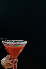 Woman hand holding red cocktail with Halloween decoration on black background. Copy space.