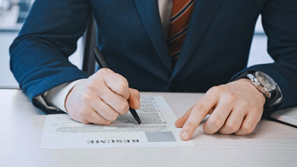 cropped view of businessman filling in resume before job interview in office.