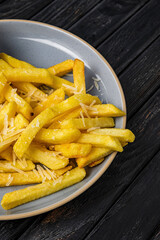 Close-up of french fries with cheese on a plate, on dark wooden backdrop