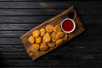 Crispy cheese nuggets with ketchup tomato sauce served on wooden board, on dark wooden backdrop