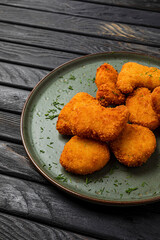 Close-up of crispy chicken nuggets on a plate on dark wooden backdrop