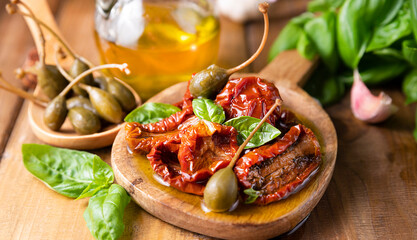 Capers and Dried tomatoes with herbs in olive oil.Large capers. Traditional appetizers in Italy with garlic, Provence herbs and basil. Ingredients for bruschetta and aperitif. High quality photo