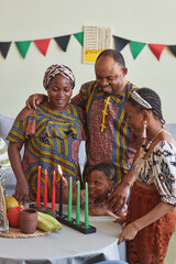 African family of four embracing and smiling while little girl burning candles for Kwanzaa holiday