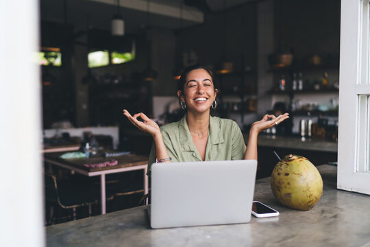 Young Happy woman enjoying work online on laptop computer holding hands in Jnana Mudra . Smiling carefree female freelancer sits at table front open netbook. Way to calm down and relax, meditation