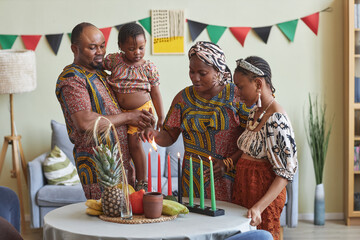 African family of four celebrating Kwanzaa at home, they lighting seven candles together on table