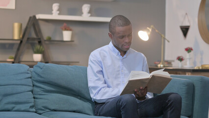 African Man Reading Book while Sitting on Sofa
