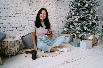 Fototapeta na wymiar Girl using smartphone near Christmas tree at home