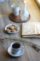 Cup of tea, plate with chocolate chip cookies, open book, reading glasses, lit candles and dry lavender flowers. Hygge at home, selective focus.