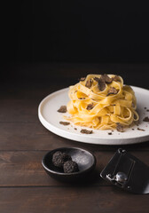Tagliatelle pasta with black truffle mushrooms. Tagliatelle al tartufo - Italian autumn fresh recipe with black truffle on the wooden table, truffle knife, rustic style, dark key, selective focus - 528552821
