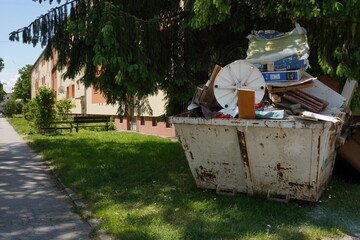 Large waste container filled with bulky waste, old furniture and other home trash. It is placed on...