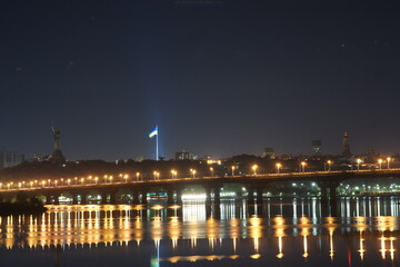 Fototapeta na wymiar KYIV, UKRAINE - SEPTEMBER 03, 2022. Beautiful view of Kiev, the capital of Ukraine. Night view across the Dnieper River. The lights of the city at night are reflected in the river