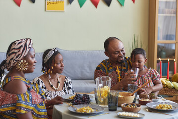 African family of four in national costumes eating traditional food and celebrating Kwanzaa holiday...