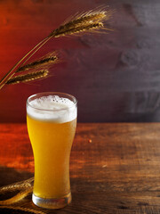 A glass of cold wheat beer on a wooden table. Ears of wheat