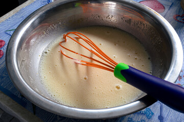 Liquid dough in an iron bowl with a whisk