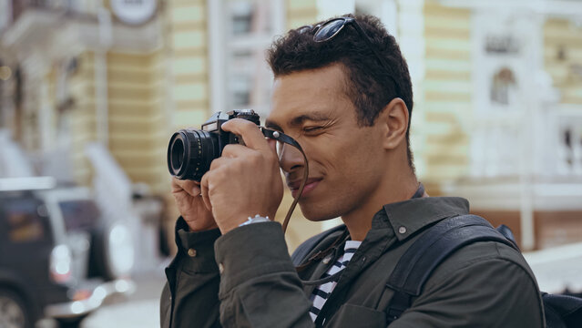 Bi-racial traveler taking photo on film camera on street.