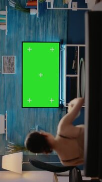 Young adult watching green screen on tv at home in modern living room. Caucasian woman having snack on couch, using mockup template display and isolated background for chroma key