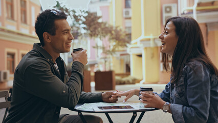 Side view of interracial couple with coffee to go holding hands near map and digital tablet on street.