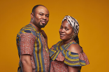 Portrait of African couple in national costumes smiling at camera standing against yellow background