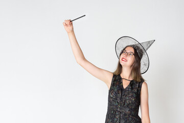 Beautiful teen girl with glasses and in a witch costume, in a hat, with a magic wand on a light...