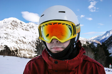 Portrait of young snowboarder in sunglass mask at the ski resort of Elbrus on the background of mountains and blue sky