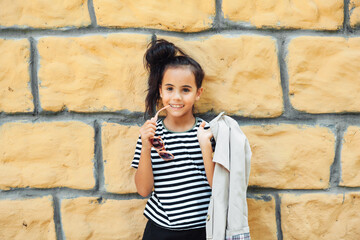 a little girl in a striped sweatshirt poses against a brick wall. children's autumn fashion. generation z