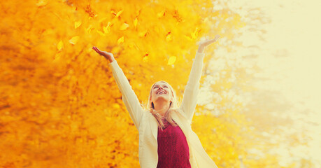 Happy smiling woman having fun with flying yellow leaves in autumn park