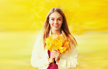 Fototapeta premium Portrait of beautiful happy smiling blonde woman with yellow maple leaves in autumn park
