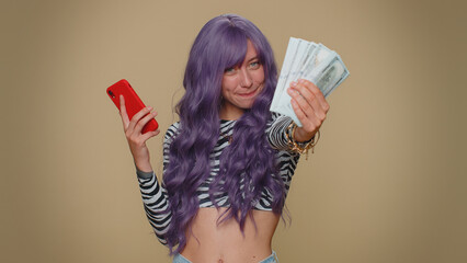 Happy young woman with lush wig looking smartphone display sincerely rejoicing win, receiving money...