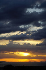 Layers of dark clouds and shiny fiery orange sunset below it