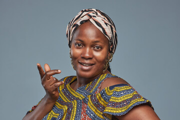 Portrait of African young woman in headscarf and national costume looking at camera against blue background