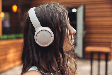 A young beautiful woman with headphones is sitting at a table in a summer cafe and drinking coffee or tea. generation z.