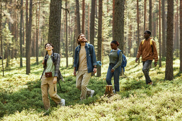 Group of friends walking along the path in the forest and looking around enjoying the nature