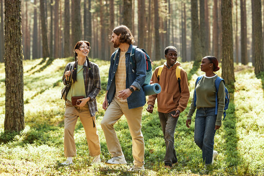Group of friends smiling and talking while walking together in the forest during their hiking