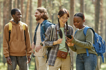 Young girls using navigator in mobile phone while they standing in forest during their traveling