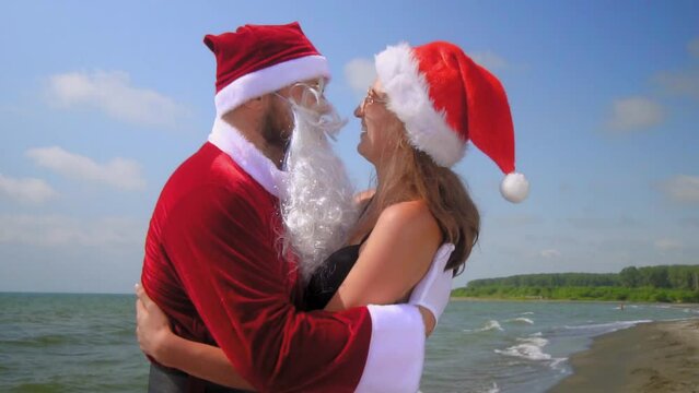 Christmas holiday. Santa Claus in a suit hugs a sexy girl in a hat in a bikini by the sea or beach. They are happy. funny and happy. Hot weather, warm and exotic climate. Stay. New Year.
