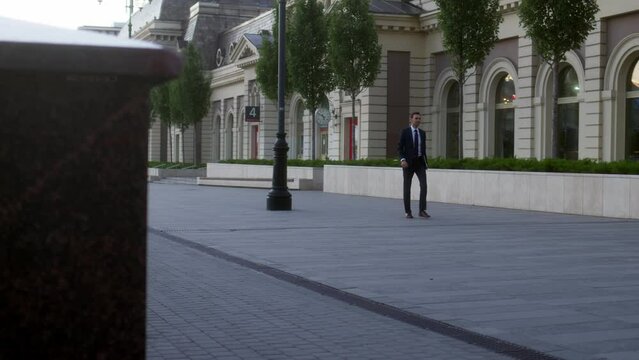 young businessman in strict blue suit with gray laptop in his hands walk down street early in morning at dawn. male office worker or big boss rushes to meeting and goes ahead.