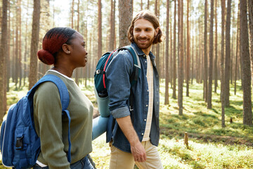 Young multiethnic couple with backpacks walking and talking together in the forest