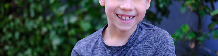 happy child on a natural green background, boy 8-9 years smiles cheerfully, lower part of the face close-up, concept of cheerful childhood, self-identification, mouth open in a smile