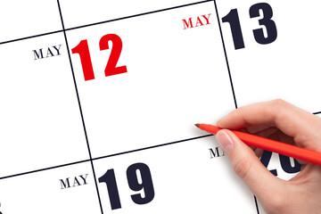 A hand holding a red pen and pointing on the calendar date May 12. Red calendar date, copy space,...