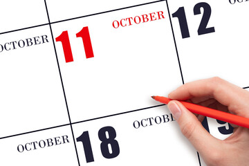 A hand holding a red pen and pointing on the calendar date October 11. Red calendar date, copy space, mockup.