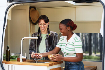 Two girls having fun in kitchen of motorhome while washing vegetables for salad under water