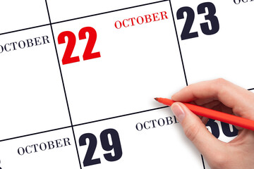 A hand holding a red pen and pointing on the calendar date October 22. Red calendar date, copy...
