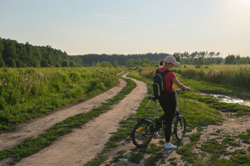 Young woman standing with bicycle and enjoying sunset in the countryside. Healthy lifestyle concept.