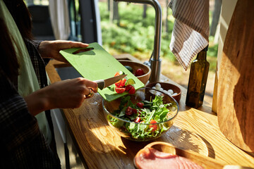 Close-up of girl putting fresh vegetable in bowl, she cooking salad in van during camping
