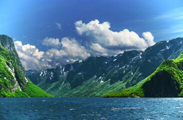 Lush green on the foot hill of snow covered mountains next to the lake, Gros Morne National Park,...