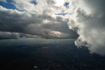 Aerial view from airplane window at high altitude of distant city covered with white puffy cumulus...