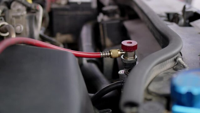 Under hood of open car lies system of manometers for refueling air conditioner. Blue pressure gauges with red and blue knobs in process of service maintenance of vehicle system.